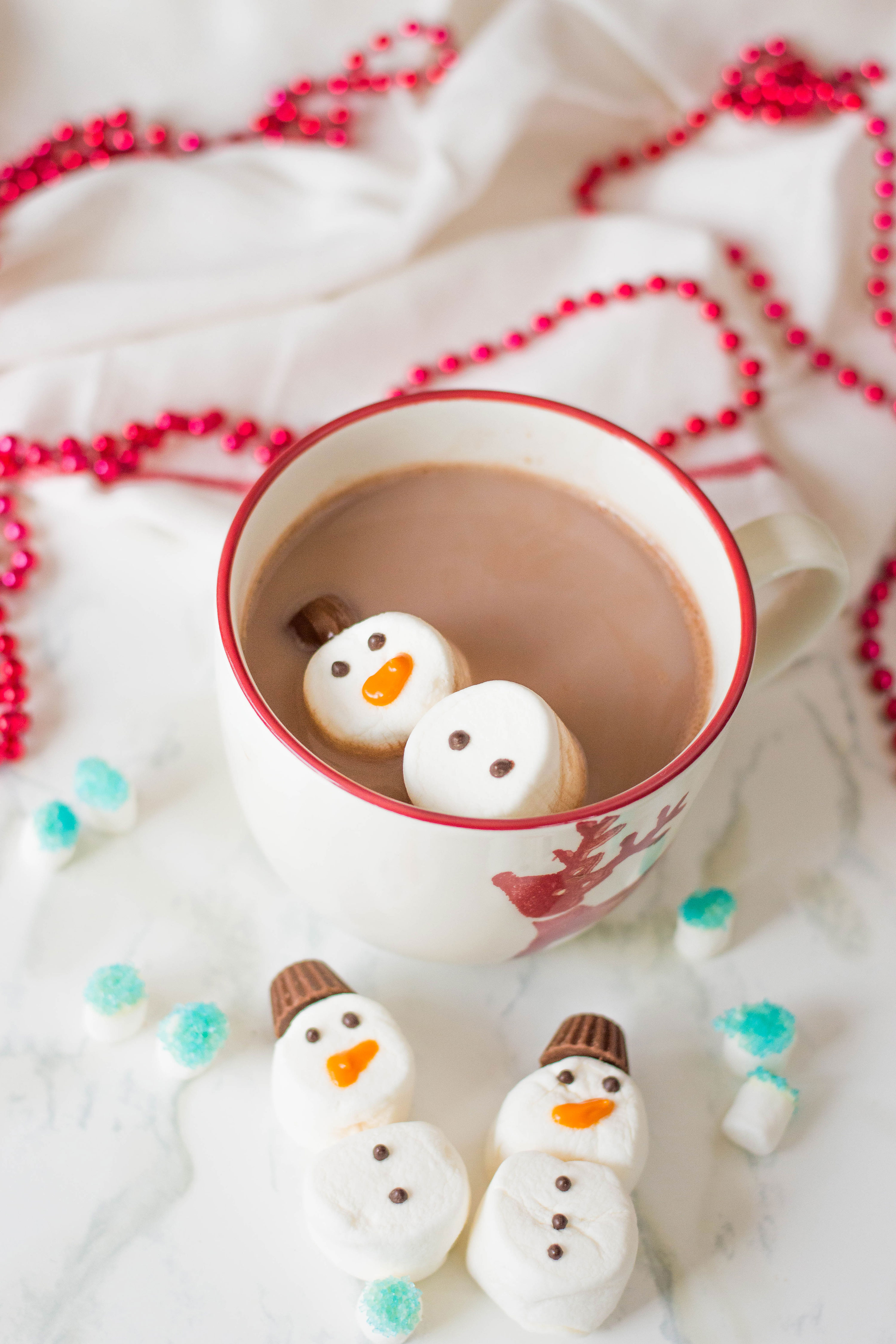 Marshmallow snowman treats floating atop a cup of hot cocoa.